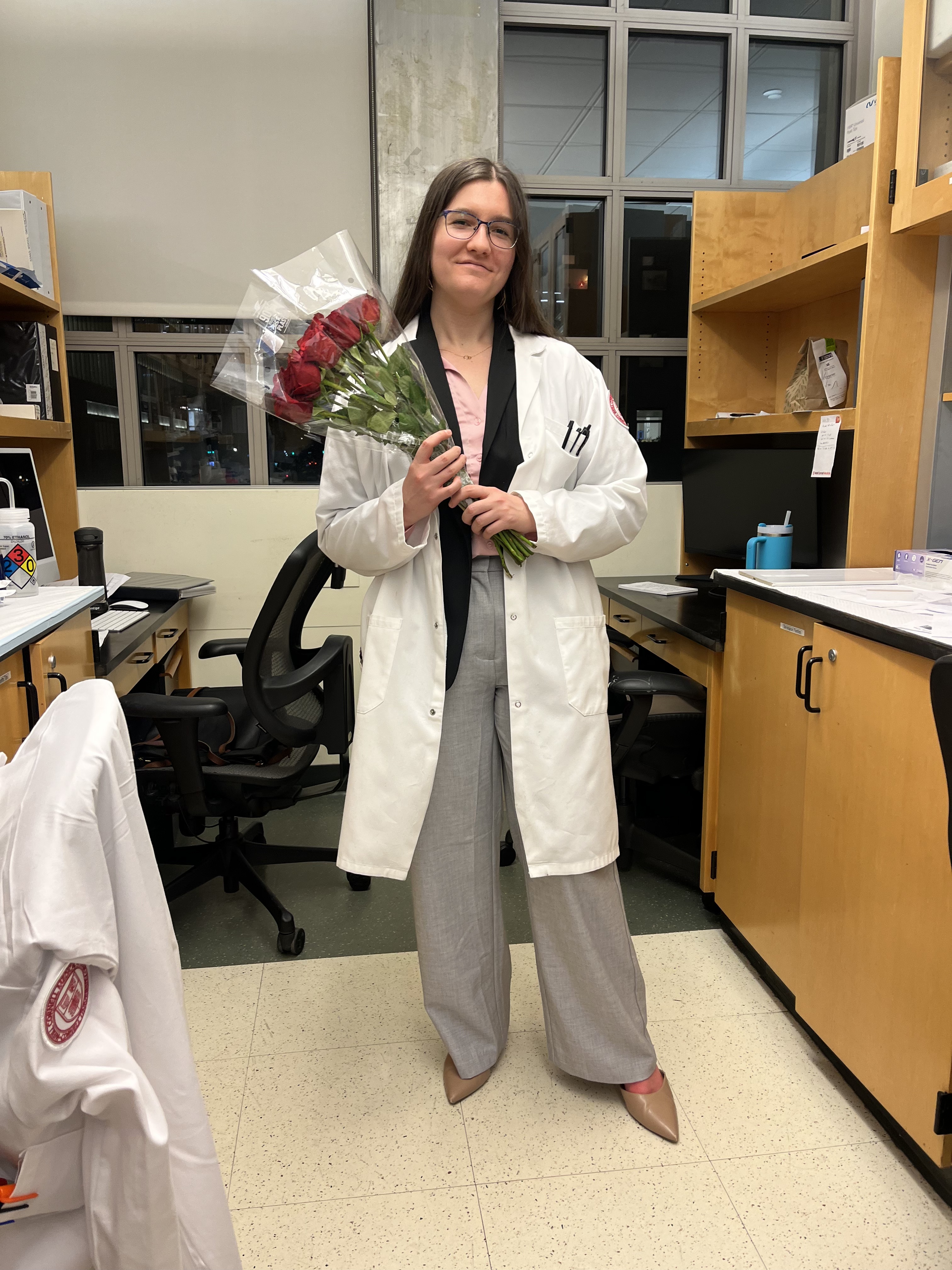 Lucy Kisova in a lab coat holding flowers to celebrate her successful thesis defense